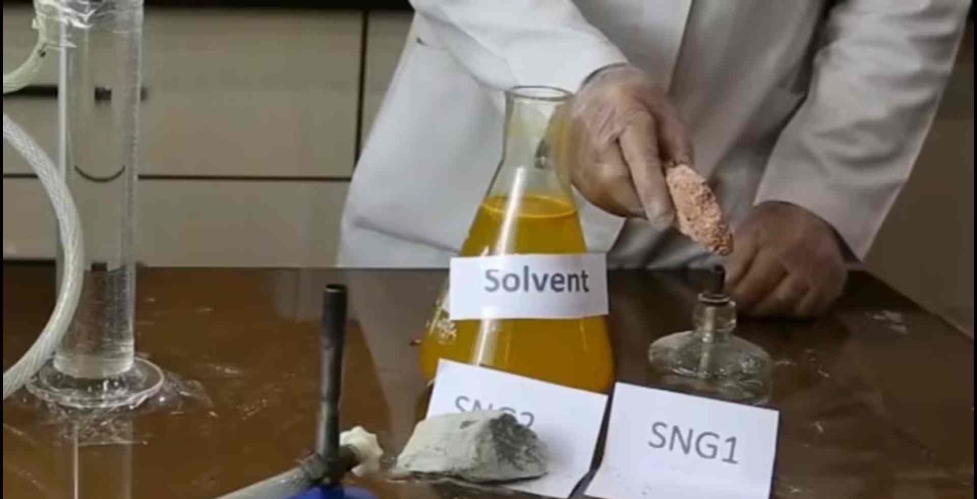 Lab technician handling solvent labeled SNG 1 with safety gloves.